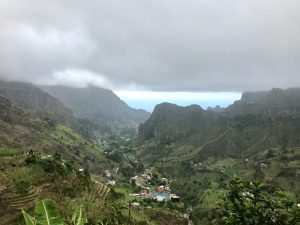 Ausblick zu Beginn des Abstiegs vom Cova Krater, dichte Wolken hängen über dem grünen Tal, in weiter Entfernung sieht man das türkise Meer